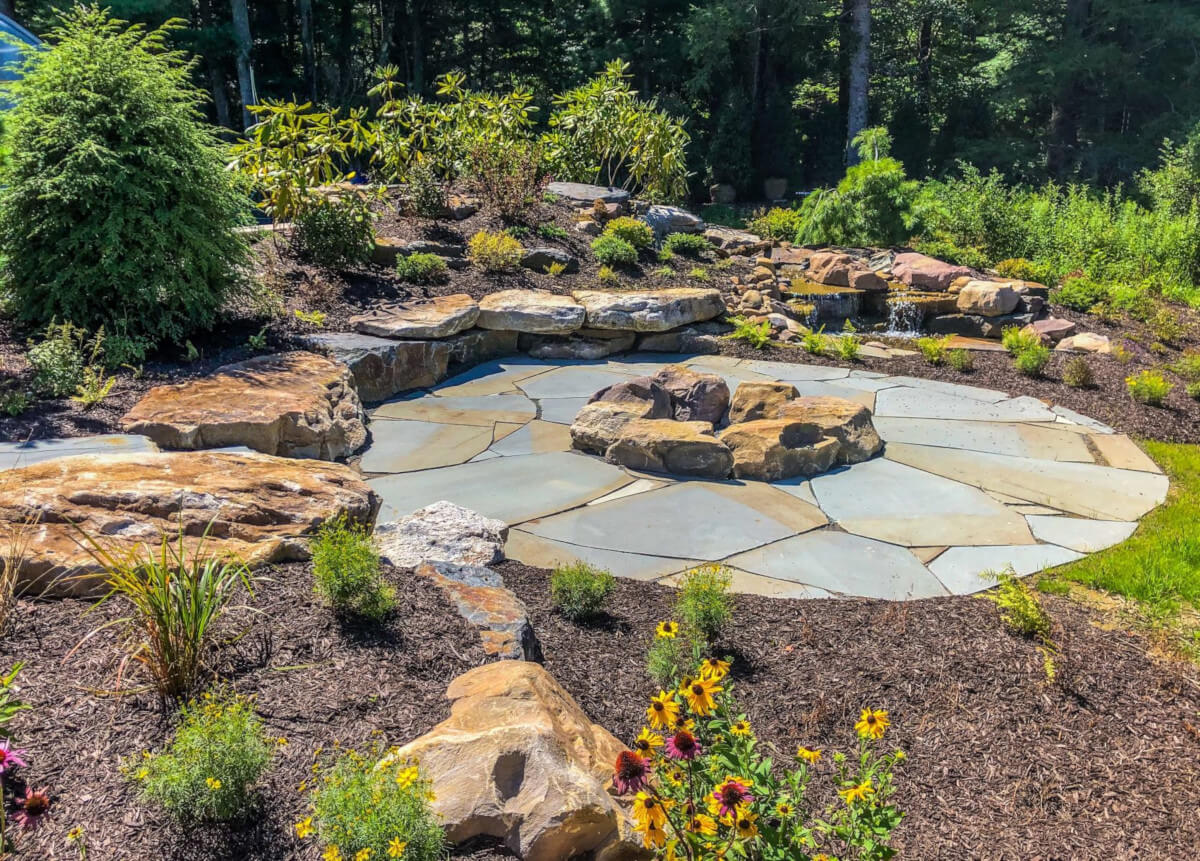 Boulder fire pit installation with gravel patio and Adirondack seating