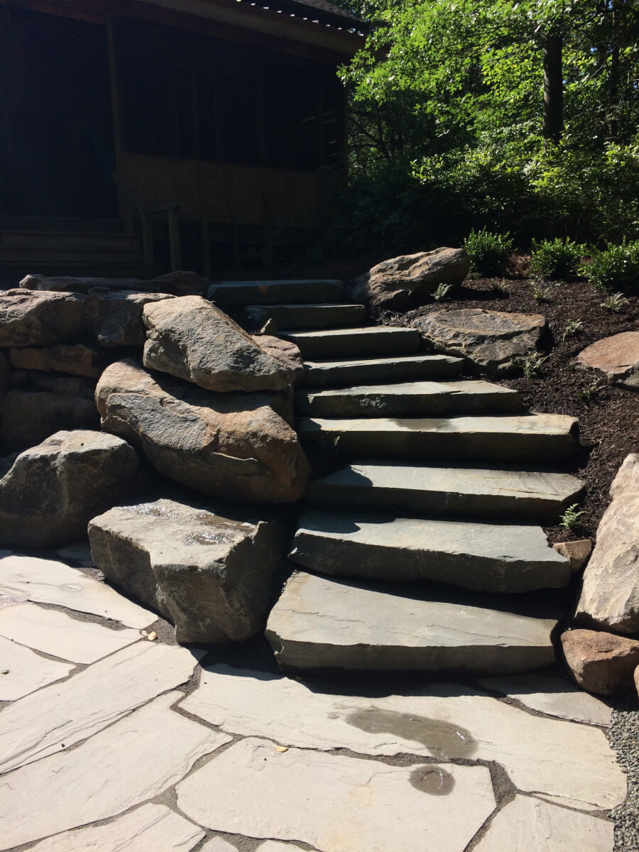 Natural stone steps with boulder retaining walls on sloped Pocono Mountains yard